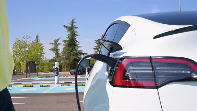 Unrecognizable african american man charging white electric car battery at public station
