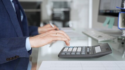 Accountant working in office, calculating finance data using black calculator and taking notes for budget planning. Audit and taxes in business