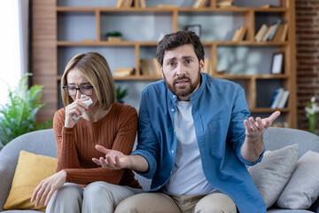 Couple in a tense online therapy session at home, woman crying, man frustrated, discussing relationship problems and seeking professional guidance via video call.