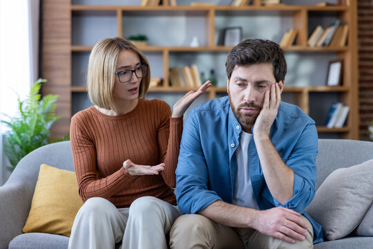 Couple having an argument on the couch, woman expressing frustration while man sits looking sad and exhausted, showing relationship problems and communication issues in their domestic setting