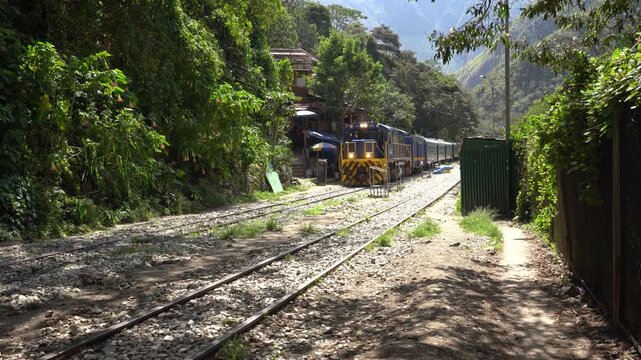 Stationary shot of a train on the rail tracks at Hidroel&eacute;ctrica station, surrounded by green trees and mountains on a sunny day in Peru