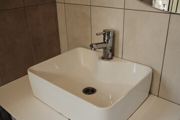 Close-up of a single white sink and chrome faucet in a clean tiled restroom interior with natural light