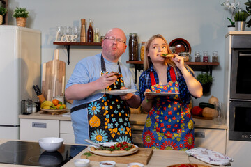 White couple sharing celebratory toast in kitchen, playful clinking of cups, aprons with floral prints, countertop snacks, relaxed evening mood, candid enjoyment