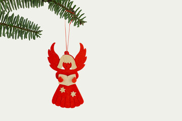 red wooden Christmas angel ornament with stars hanging from a pine branch on a white background
