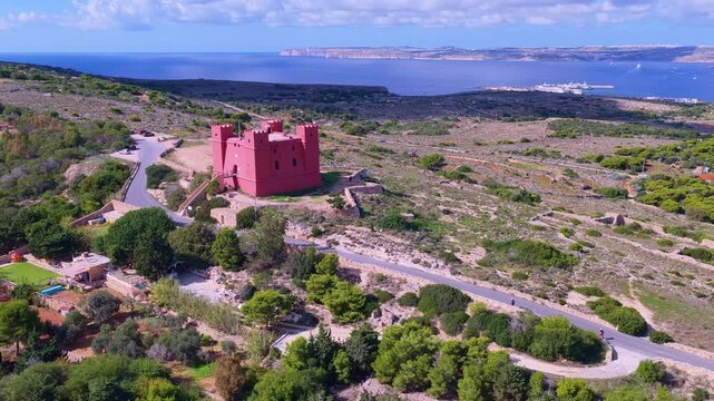 Cinematic 4K drone flight soars over the iconic Red Tower (St. Agatha's Tower) in Mellieha, revealing a breathtaking panorama of Mellieha Bay and the distant island of Gozo