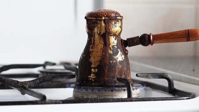 Male Hand Holding Traditional Coffee Turk with Overflowing Coffee on Stove Flame