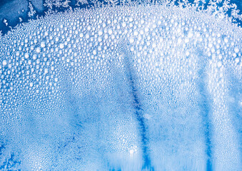 Abstract frozen ice texture with frost crystals and condensation droplets on blue glass surface