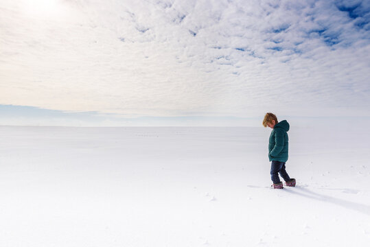 Side view of a young Boy wearing a puffer jacket walking in deep snow in the countryside, USA