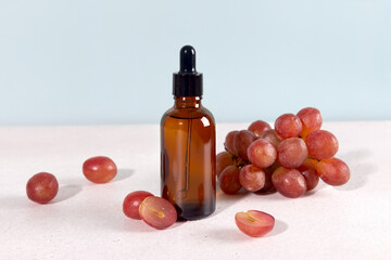 Grape seed oil in dropper bottle with fresh green grapes on a blue background. Skin care concept.