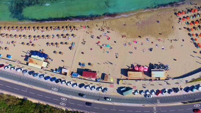 Midday 4K drone reveal over Mellieha Bay, Malta: rows of umbrellas and sunbeds, clear turquoise water, shoreline activity and beachfront amenities &mdash; ideal for travel, tourism and lifestyle