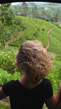 Young curly haired woman enjoying the scenic view of sri lankan tea plantations from a moving train window, her hair blowing in the wind during a memorable and adventurous journey