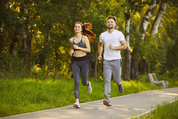 Obraz premium Couple family running happily together, man and woman jogging on park path near green trees, shared exercise, healthy lifestyle partnership, outdoor fitness and enjoyment, positive active nature sport