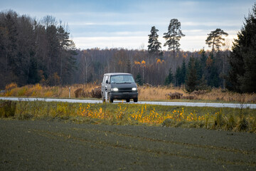 Van driving on countryside road through autumn landscape, rural travel and transportation concept...