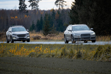 Two cars driving on countryside road through autumn forest, transportation and travel concept,...