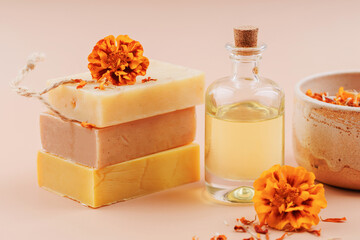 Stack of handmade soap bars with fresh marigold flower, glass bottle of calendula oil and dried petals on pastel background