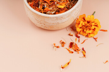 Closeup of dried marigold petals in ceramic bowl with fresh tagetes flower and herbal fragments on...