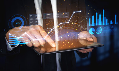 A businessman interacts with a digital tablet showcasing financial graphs and data metrics,...