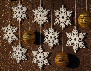 White crochet snowflakes hanging with golden balls on brown background.