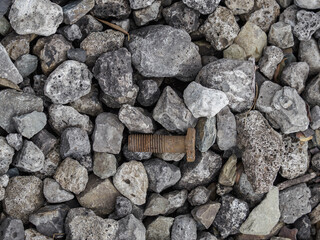An old rusty bolt lying among the stones of a drainage ditch.
