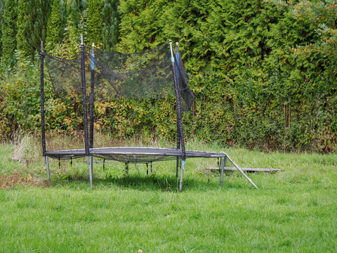A view of a broken outdoor trampoline in the grass in a garden.
