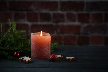 Red candle and some Christmas decorations against a brick wall, light in the dark for Christmas, Advent or New Year, copy space, selected focus