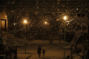 Daily Life in Japan 
Mother and young child walking through a small city park on a snowy evening