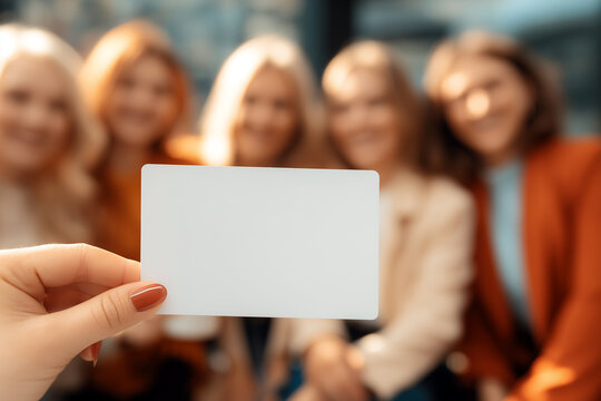 A close-up shot of a hand holding a blank white card mockup against friends in the background