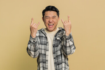 Naklejka premium Overjoyed happy Asian middle-aged man showing rock n roll gesture by hands cool sign shouting yeah with crazy expression, dancing, rejoicing victory win success. Mature Chinese guy on beige background