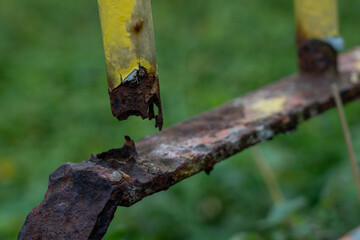 Extreme close-up showing a section of a heavily rusted metal frame or pipe, where the original yellow paint has flaked away, revealing deep corrosion and decay
