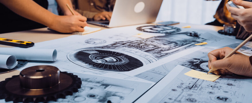 A vibrant scene capturing a collaborative engineering session where team members engage with technical drawings and sketches spread across a modern workspace table. SACTR - Powered by Adobe