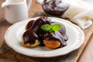 Delicious profiteroles with chocolate and white plate. Selective focus image on light background.