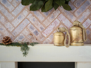 Brick fireplace hearth mantle Christmas holiday festive decoration with metal vintage brass bells and greenery, hanging green wreath and white wood shelf.