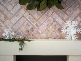 Brick fireplace hearth mantle Christmas holiday festive decoration with cutout snowflakes and greenery, hanging green wreath and white wood shelf.