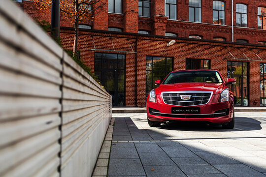 Red Cadillac ATS sports sedan parked on road daytime in front of brick building American automotive performance luxury urban street scene modern vehicle