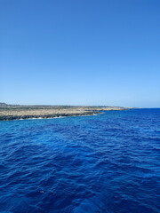 The Stunning Blue Ocean is complemented with Clear Skies above and a Rocky Shoreline nearby