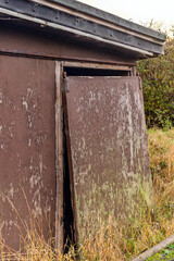 Sliding plywood door with brown peeling paint that has come off its track on an old abandoned farm building