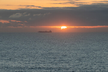 Naklejka premium Beautiful sunset over ocean with cargo ship sailing near horizon in calm waters