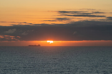 Fototapeta premium Beautiful sunset over ocean with cargo ship sailing near horizon in calm waters