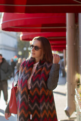Young beautiful woman in grey coat and red scarf walking along the street