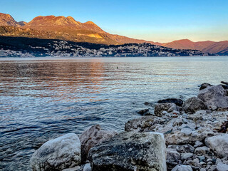 golden illuminated shoreline with mountain background, calm bay with textured rocks and shimmering