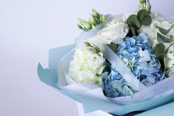 Elegant bouquet of white roses and blue hydrangeas with eucalyptus leaves, wrapped in pastel blue paper
