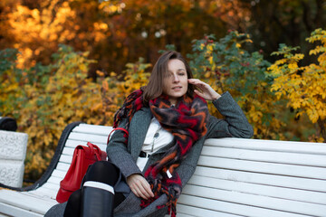 Beautiful business woman in a cozy scarf on an autumn park bench