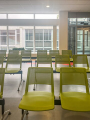 Modern hospital corridor featuring clean, spacious waiting area with green chairs and large windows, designed for comfort and rest in a contemporary healthcare environment