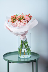 Elegant bouquet of white hydrangeas, pink carnations, and red berries wrapped in pastel pink paper, placed in a glass vase
