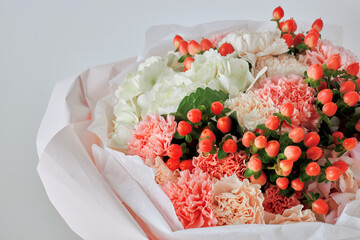 Close-up of a romantic bouquet with peach and pink carnations, white hydrangeas, and red hypericum berries in soft pink wrapping
