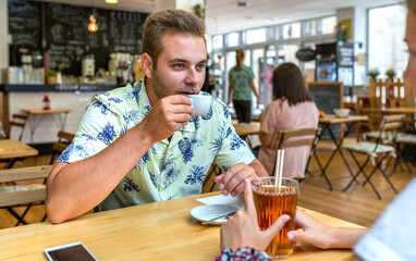 Young man wearing a casual shirt, relaxing and enjoying coffee while sitting with a companion at a wooden table in a cafe, creating relaxed atmosphere and a sense of connection