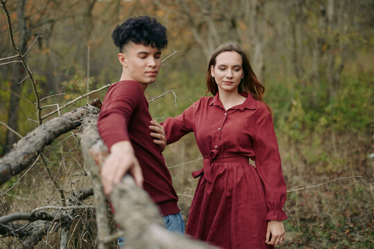 Authentic portrait of a young couple sharing a quiet moment by a rustic fence in autumn woods, natural expressions and genuine connection conveying trustworthiness and warmth.