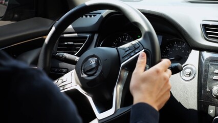 Male arms holds steering wheel while driving a motor car at city. Young man operating the...
