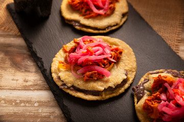 Panuchos, a typical dish from Yucatan, Mexico. A handmade, fried corn tortilla filled with beans, topped with cochinita pibil, pickled red onion, and habanero pepper.