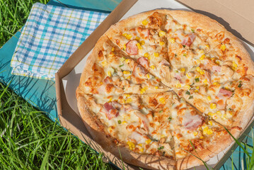 Pizza in a box on the grass. Food delivery. Pizza with chicken, bacon, corn.